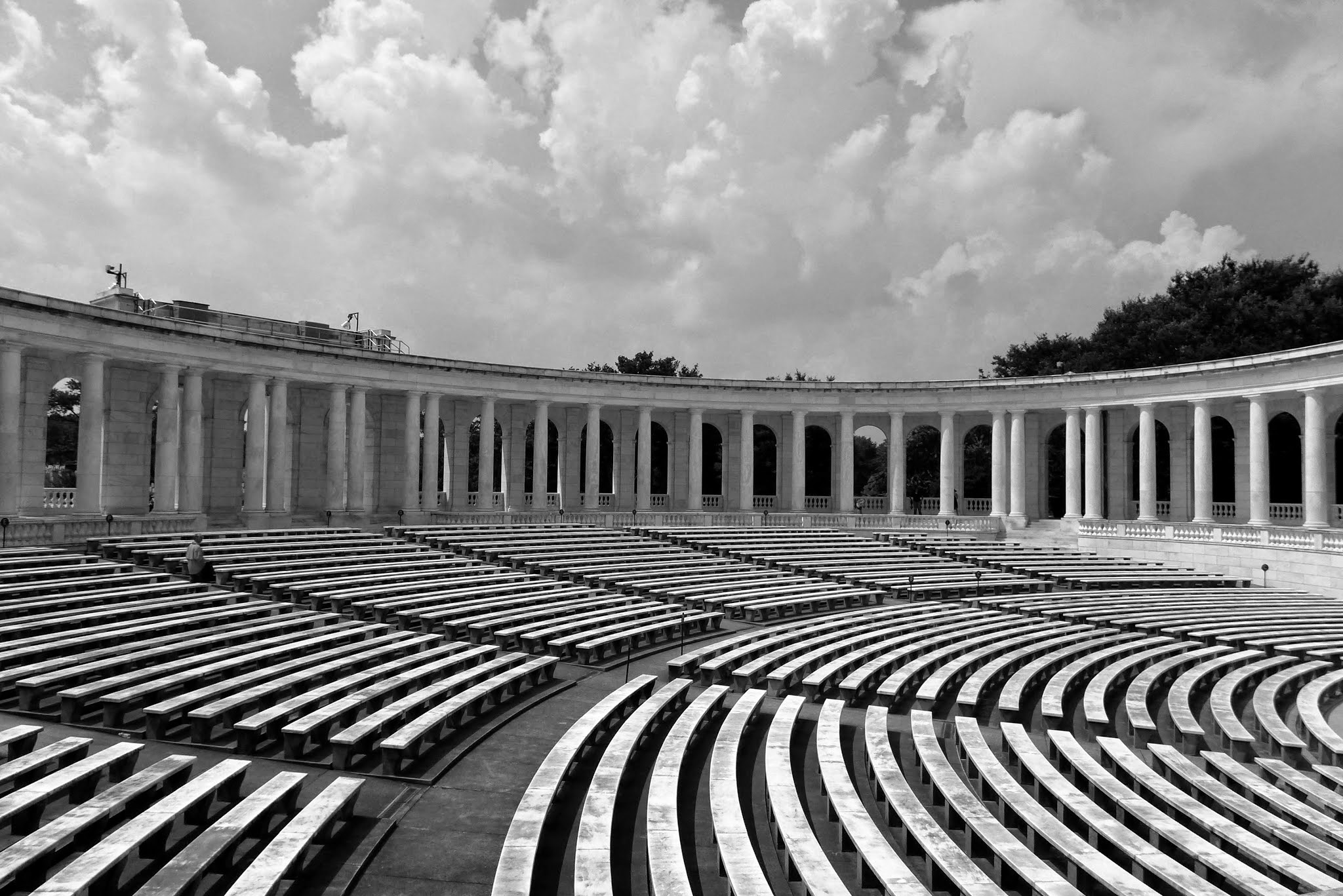 Black and white photo of the semicircular Memorial Amphitheater colonnade at Arlington National Cemetery with rows of marble benches